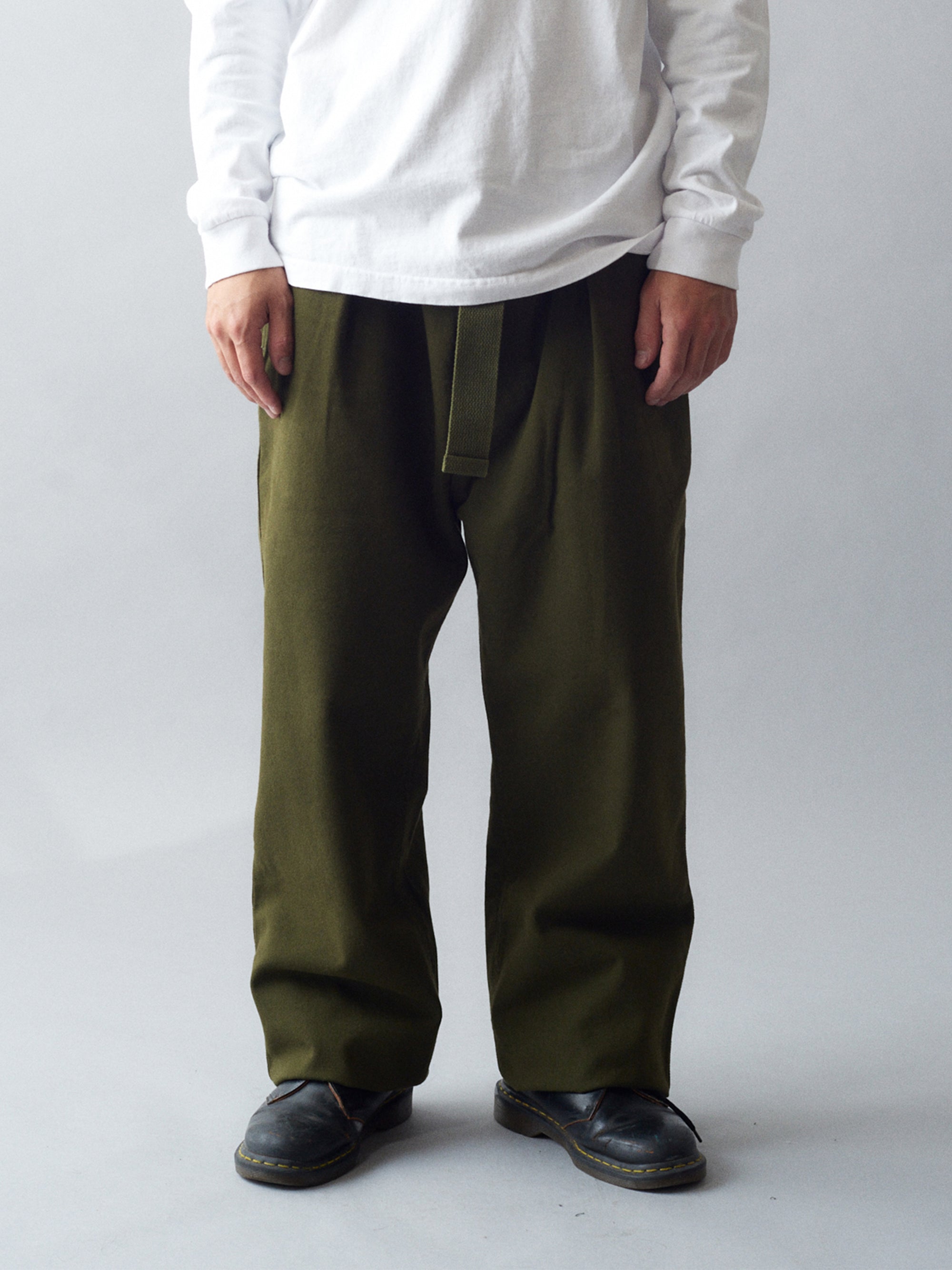 Man wearing MHL Cotton Wool Drill Slide Adjuster Trouser in olive green standing against a grey background.