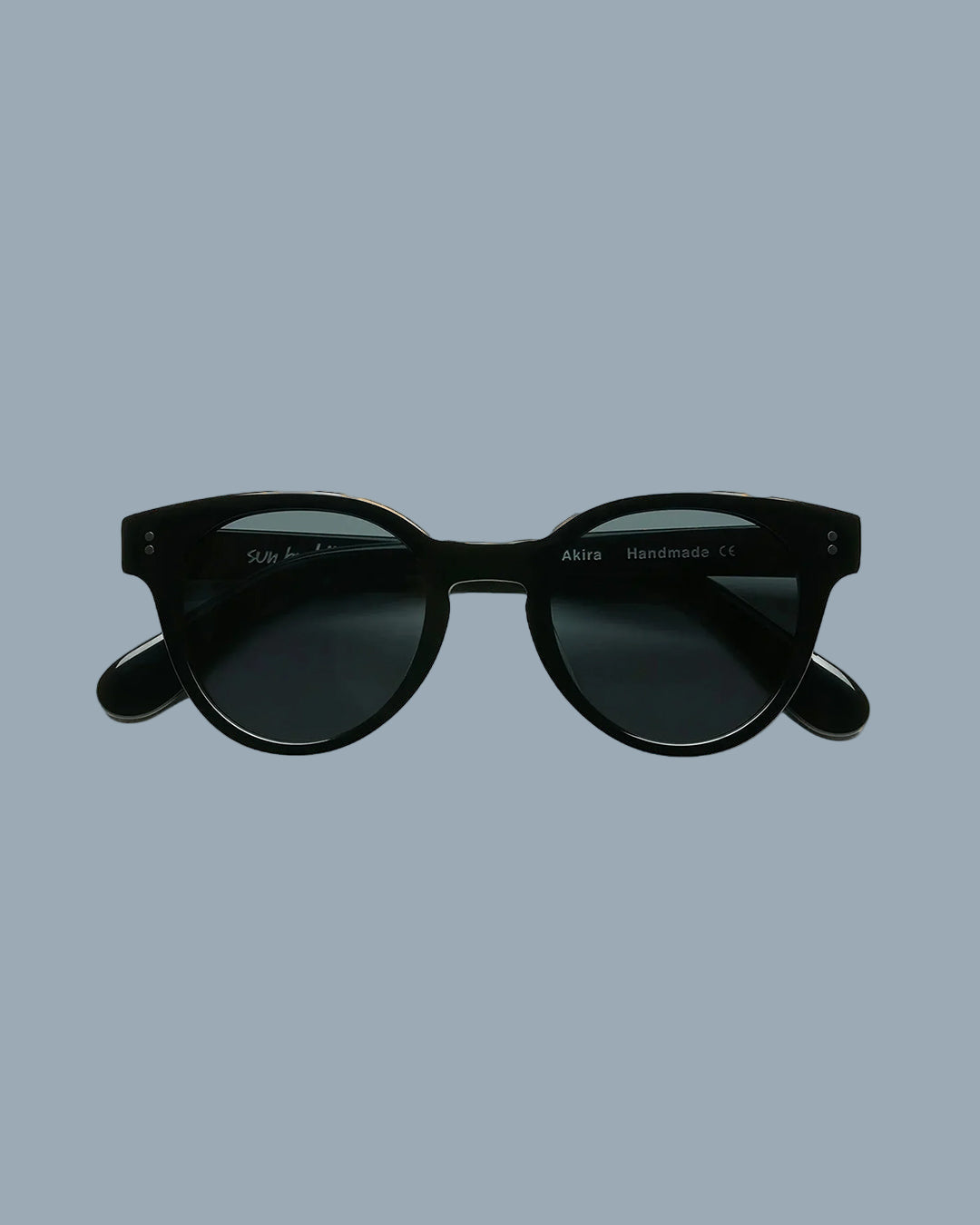 A pair of round frame acetate sunglasses in black color, displayed against a beige background.